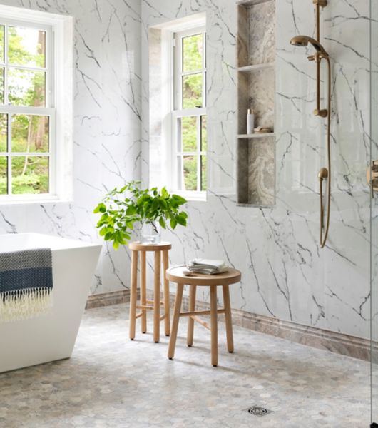 This spacious bathroom features white marble-look tile with dark grey veining and hexagon-shaped travertine tile floor.