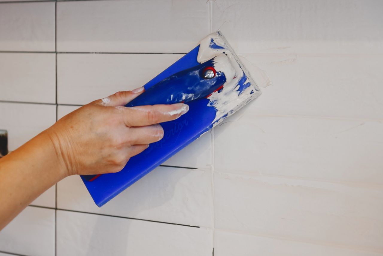 Using a grout float to apply grout to a white subway tile kitchen backsplash.