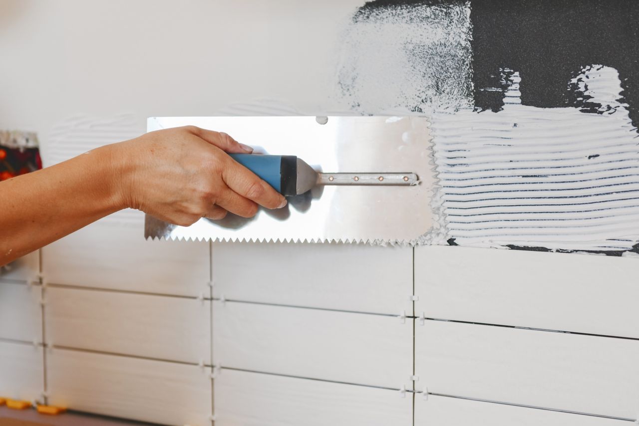 Using a notched trowel to apply tile adhesive to a kitchen wall before laying tile.