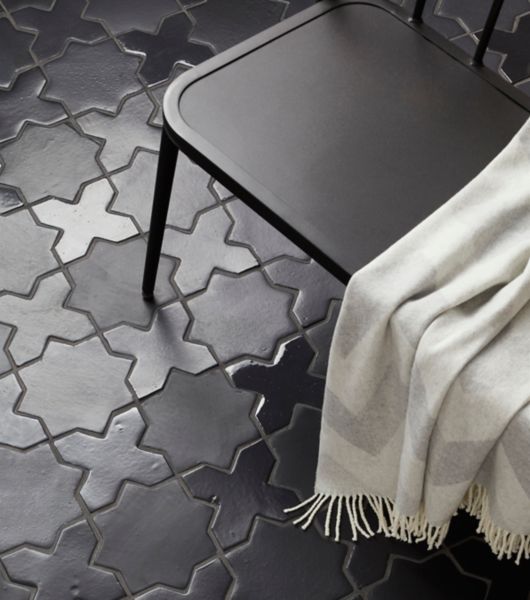 A tile floor is covered in black Zellige tiles. Eight-pointed stars in a matte finish and cross-shaped pieces in a gloss finish fit together to create a uniform floor covering with understated pattern.