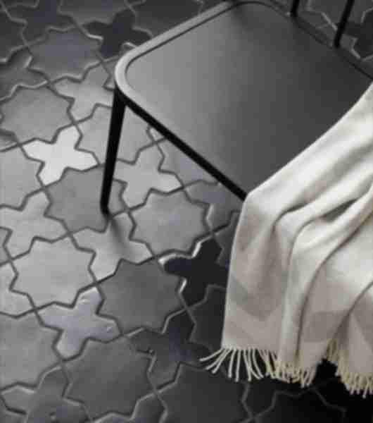 A tile floor is covered in black Zellige tiles. Eight-pointed stars in a matte finish and cross-shaped pieces in a gloss finish fit together to create a uniform floor covering with understated pattern.