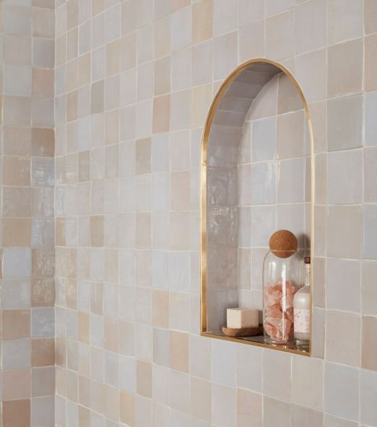 A bathroom shower wall and recessed storage niche feature Zellige tile. The niche is arch-shaped and framed in gold-tone trim.