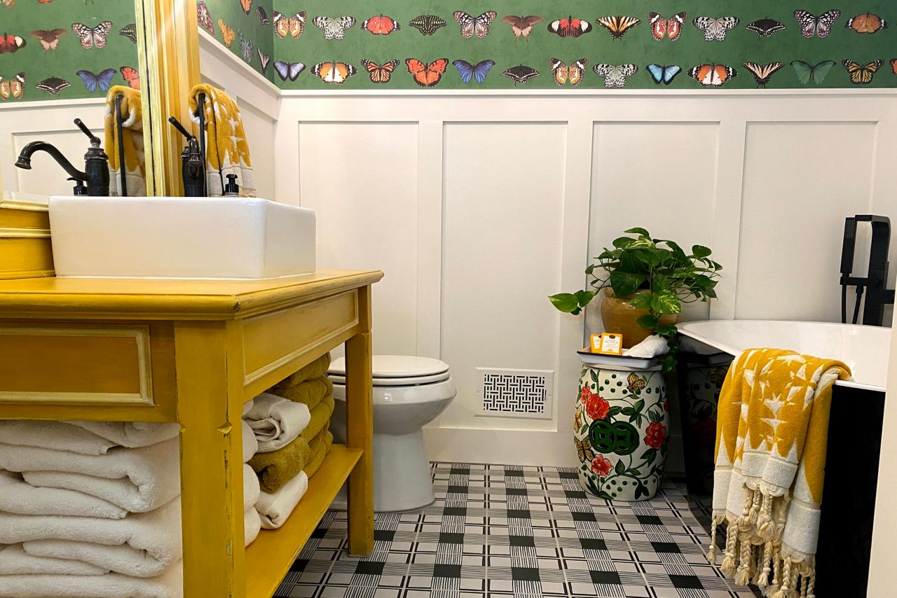 This bright and cheery bathroom features a black-and-white patterned tile floor and butterfly wallpaper. 