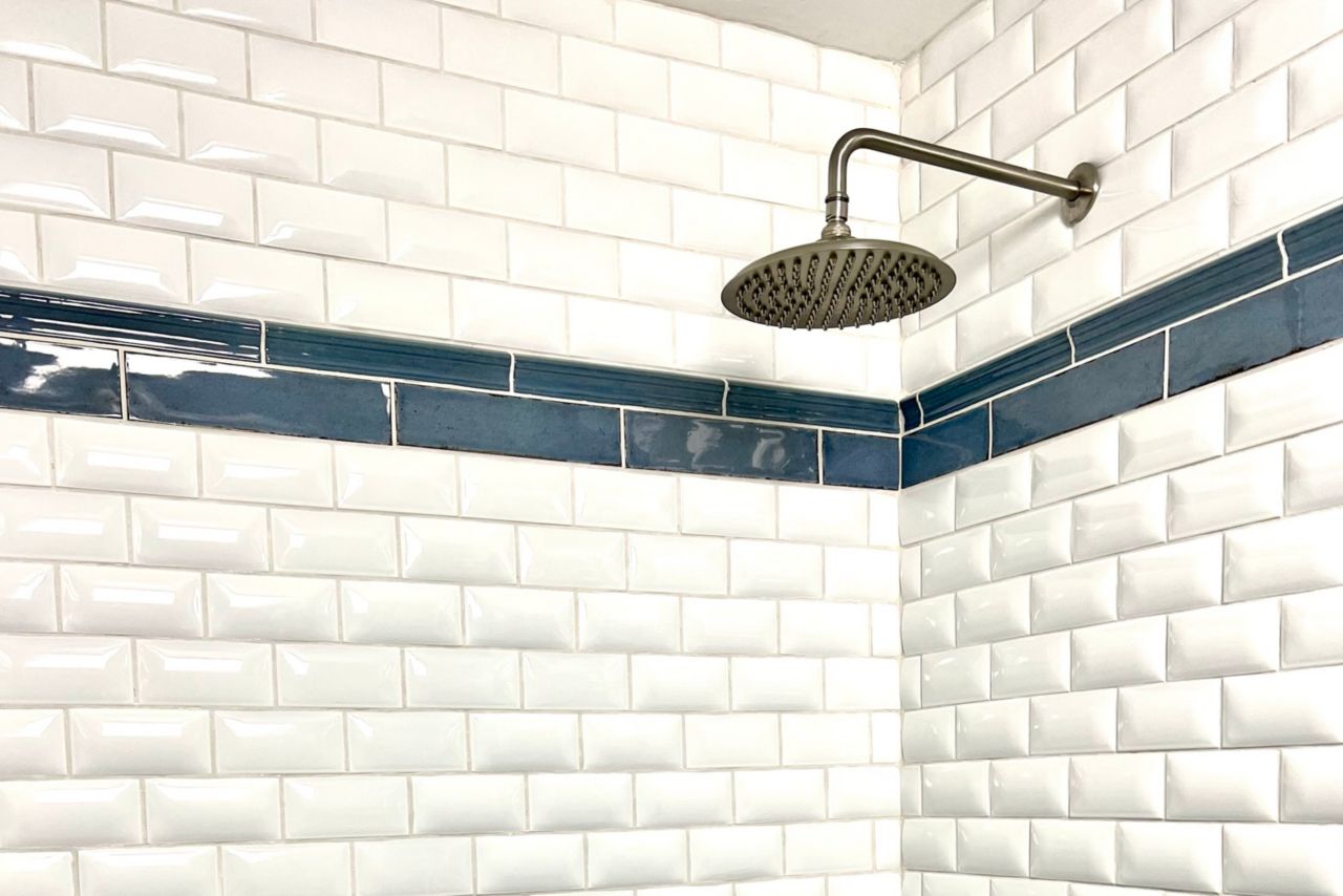 A corner shot of a shower with white subway tile with a raised, puffed surface and a band of blue handmade-look subway tile.