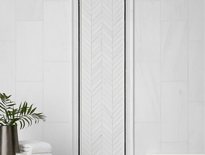 White marble wall tile with chevron accent design and black trim in modern bathroom.