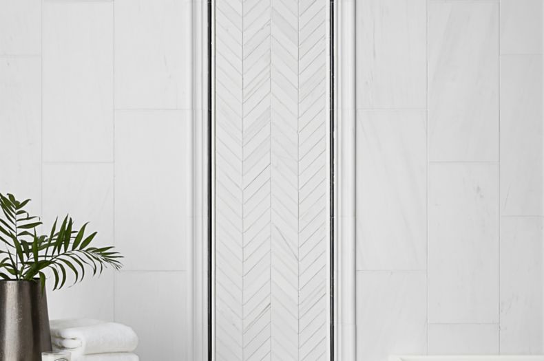 White marble wall tile with chevron accent design and black trim in modern bathroom.