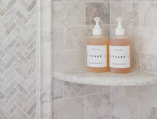 Shampoo and soap bottles on beautiful brushed white marble corner shelves in a shower.
