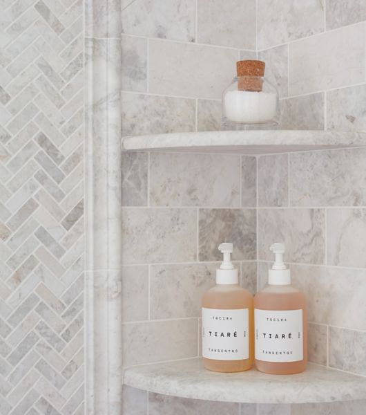 Shampoo and soap bottles on beautiful brushed white marble corner shelves in a shower.