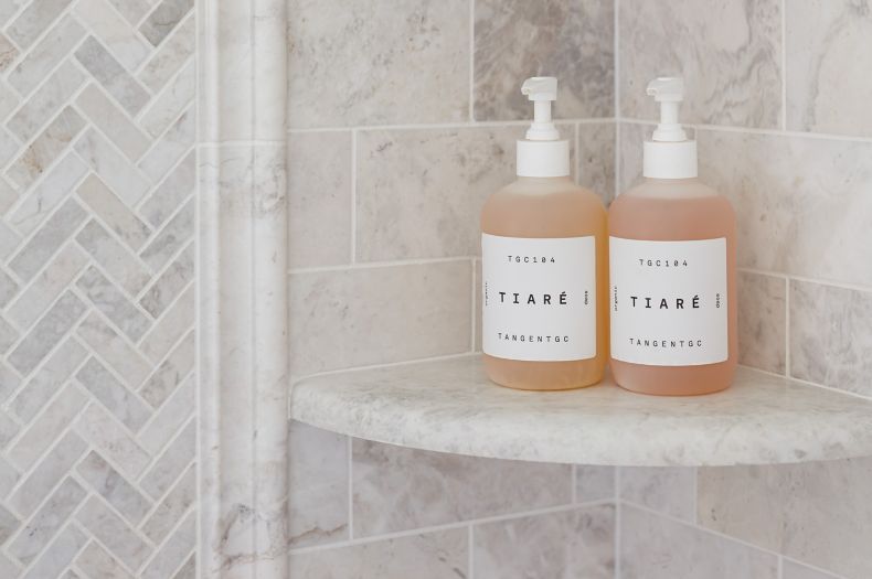 Shampoo and soap bottles on beautiful brushed white marble corner shelves in a shower.