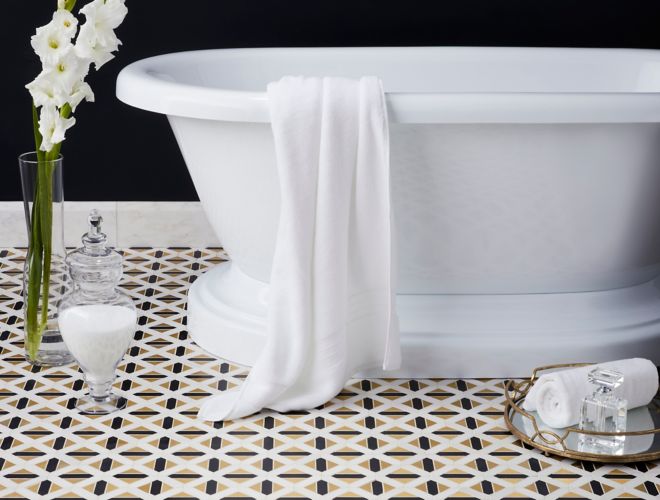 Gold black and white geometric floor tile in glamorous bathroom with freestanding tub. 