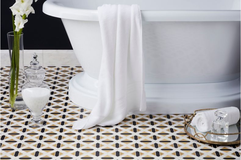 Gold black and white geometric floor tile in glamorous bathroom with freestanding tub. 