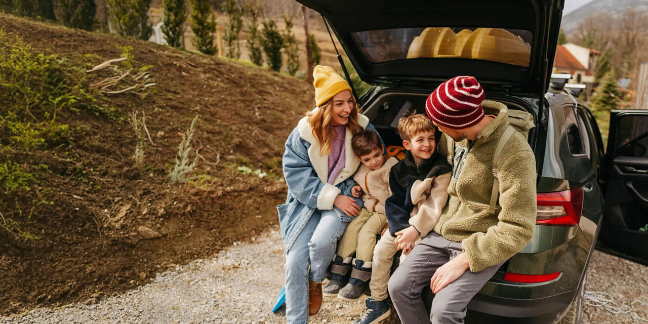 Family taking a break at the open tailgate of an SUV during a road trip.