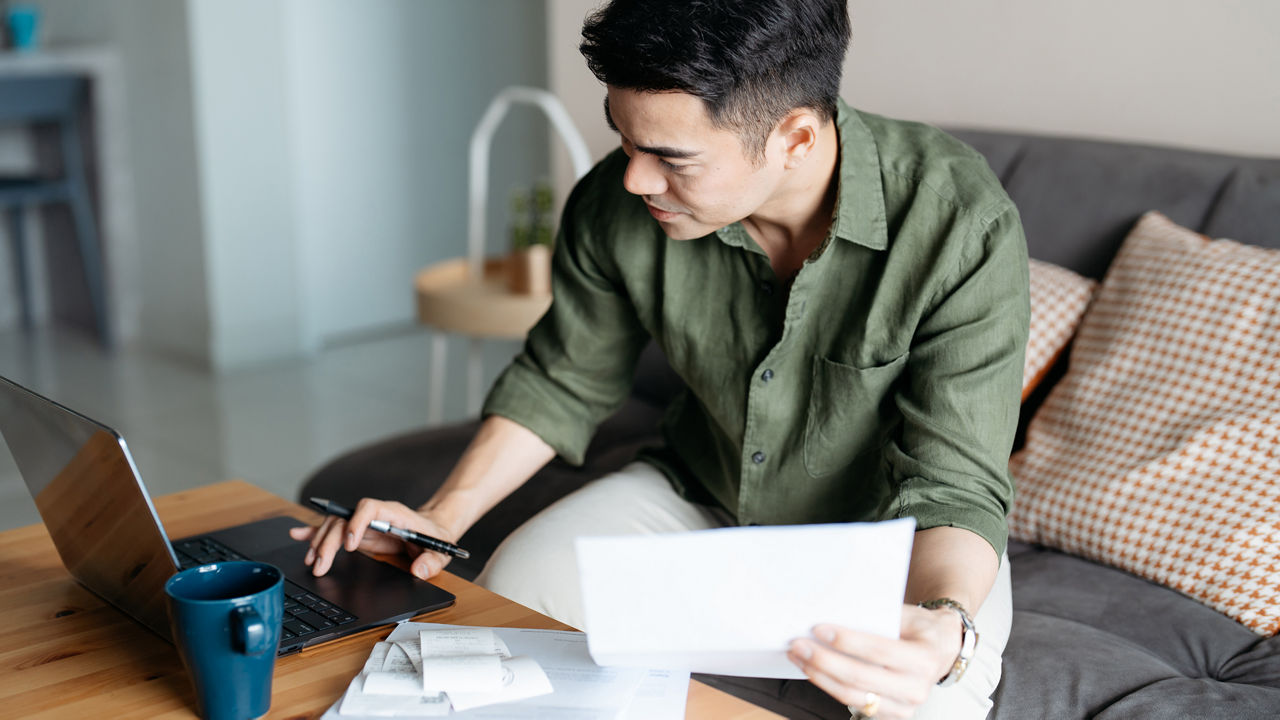Person reviewing bills and documents while using a laptop at home.