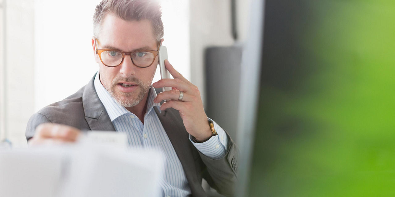 Personne parlant au téléphone cellulaire tout en consultant des documents dans un bureau.