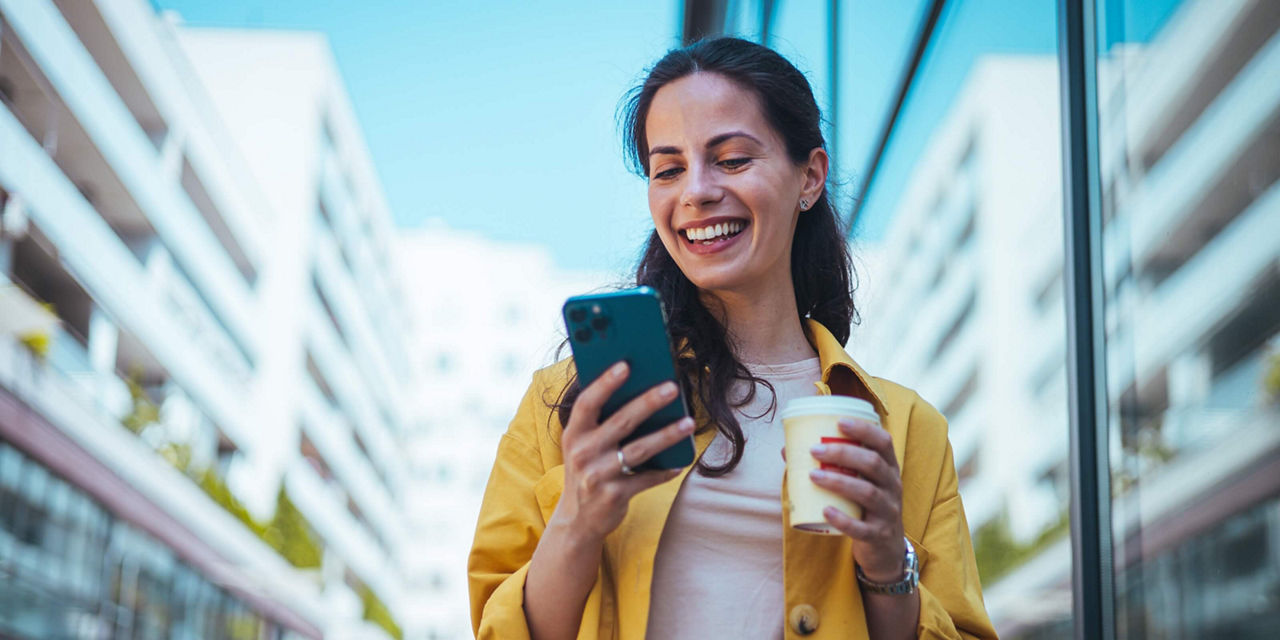 Person using a smartphone while holding a beverage in an urban setting.