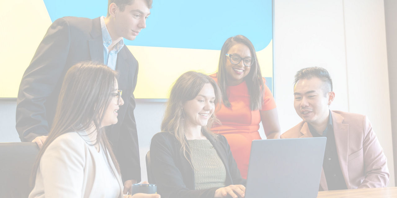 Team members gathered around a laptop during a workplace meeting.