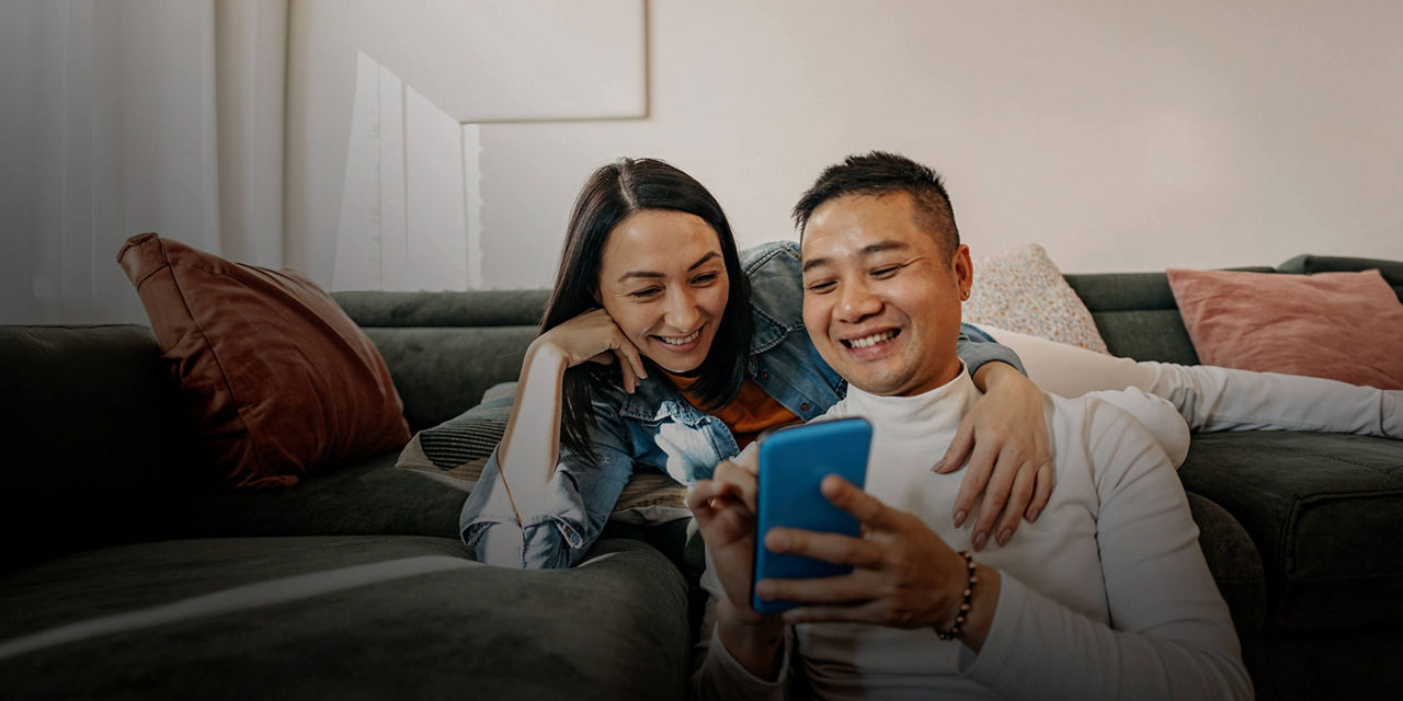Deux personnes se détendent à la maison en utilisant un téléphone intelligent sur un canapé.