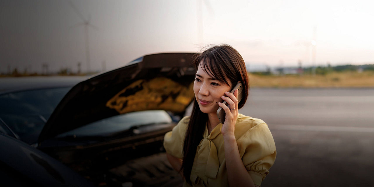 Driver making a phone call beside a vehicle with the hood open.