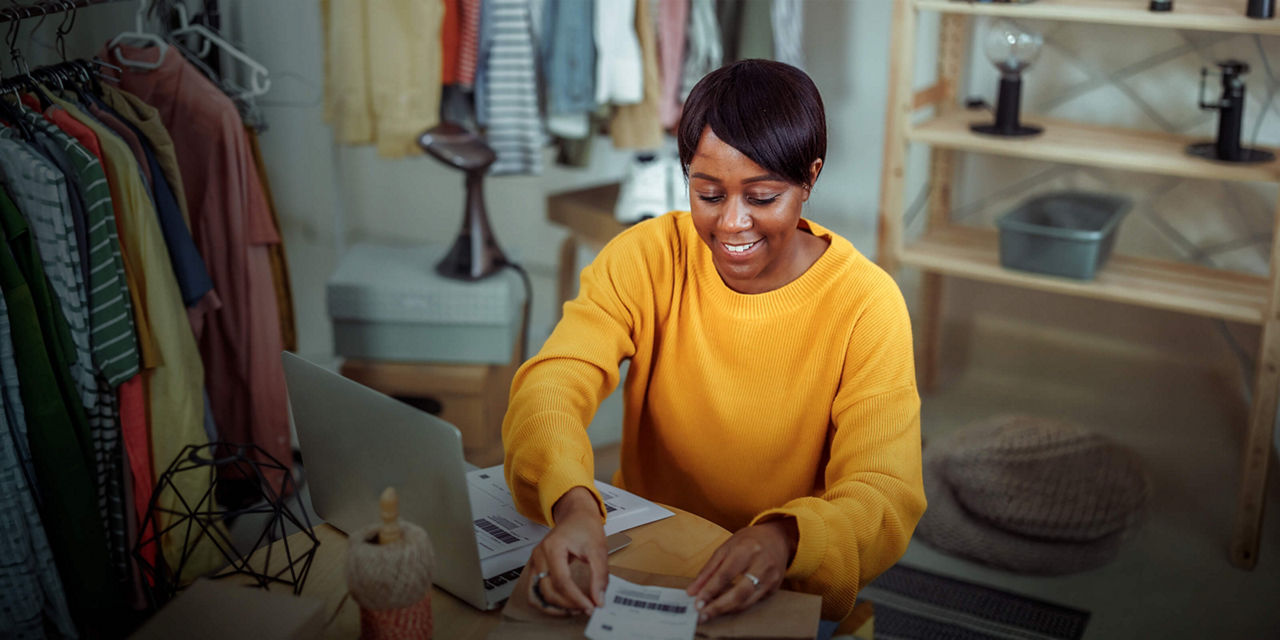 Person packaging products at home while working on a laptop for a home-based business.