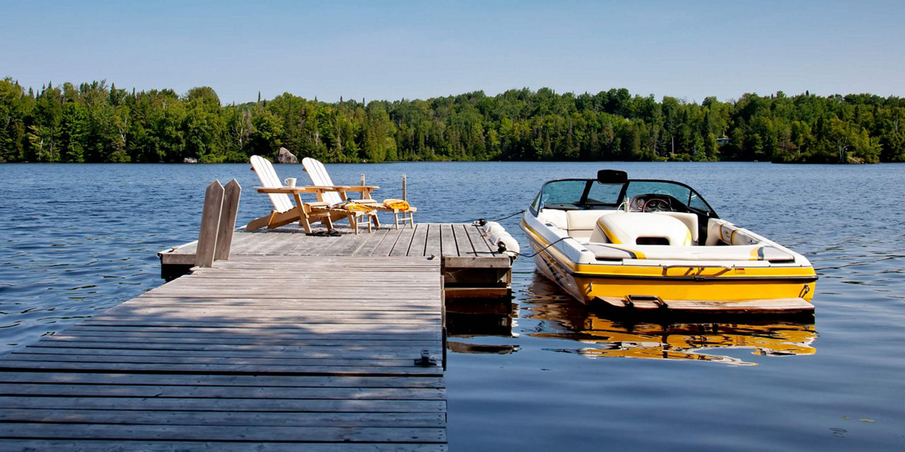 Motorboat docked beside a wooden pier on a calm lake.