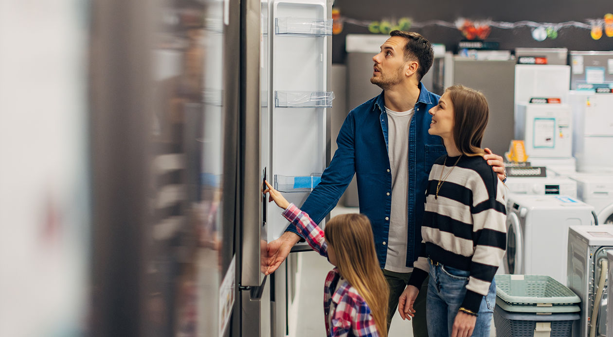 Cheerful parents and daughter choose a refrigerator in the home appliance section of a wholesale store.