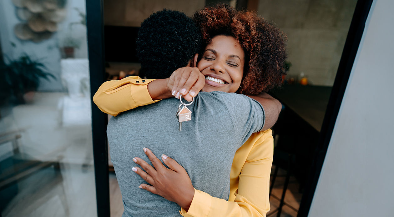Man and a women couple, hugging tightly in a doorway. The woman is holding keys. 