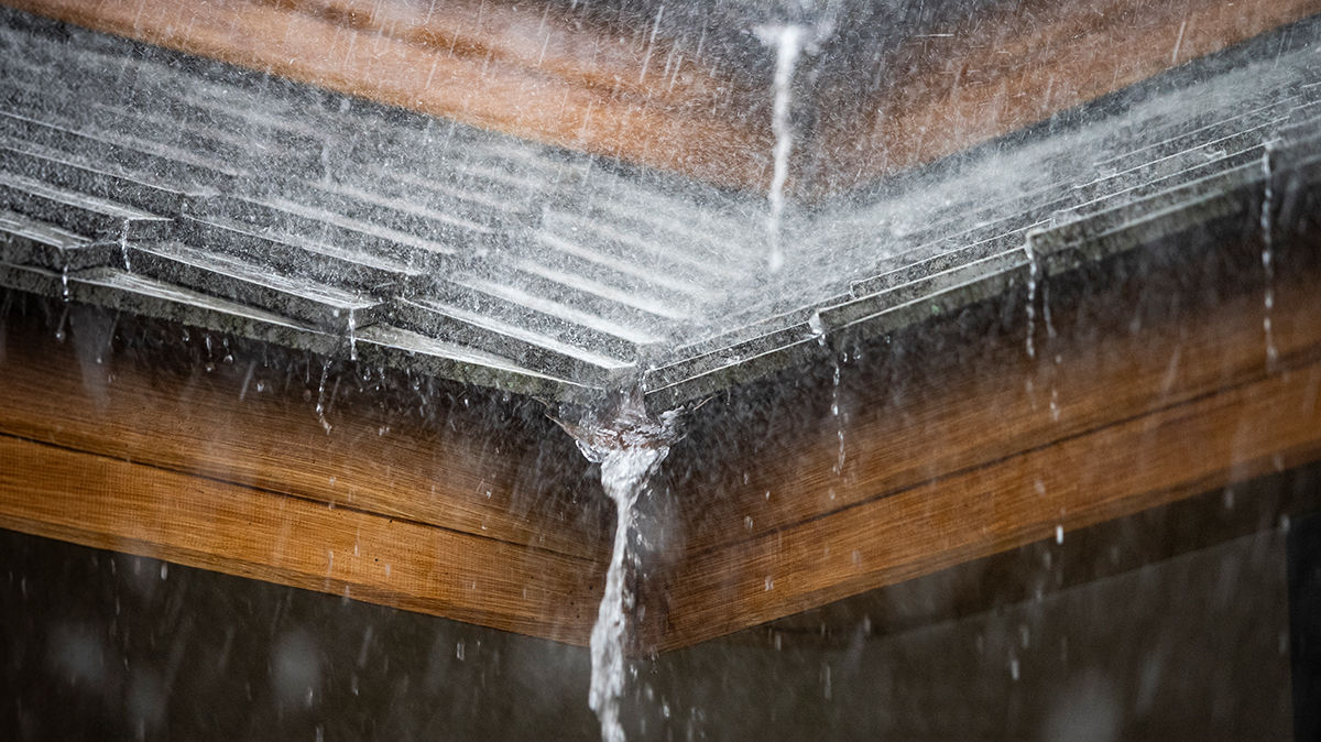 Close-up of extreme rainfall on a shingled roof valley, with rain pouring over the edge. 