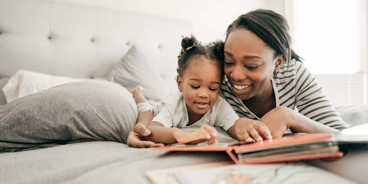 Adult and child reading a book together on a bed.
