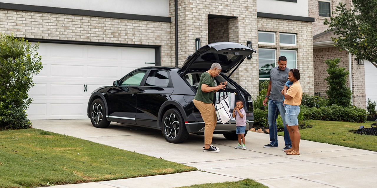 Family unloading items from an electric SUV in the driveway of their home.