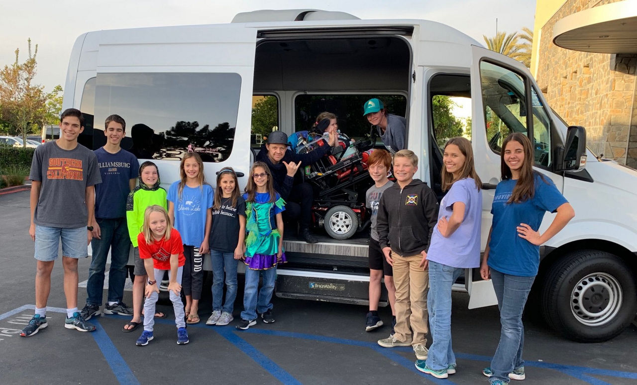 Group of students outside of a commercial bus with a BraunAbility wheelchair lift next to an access aisle