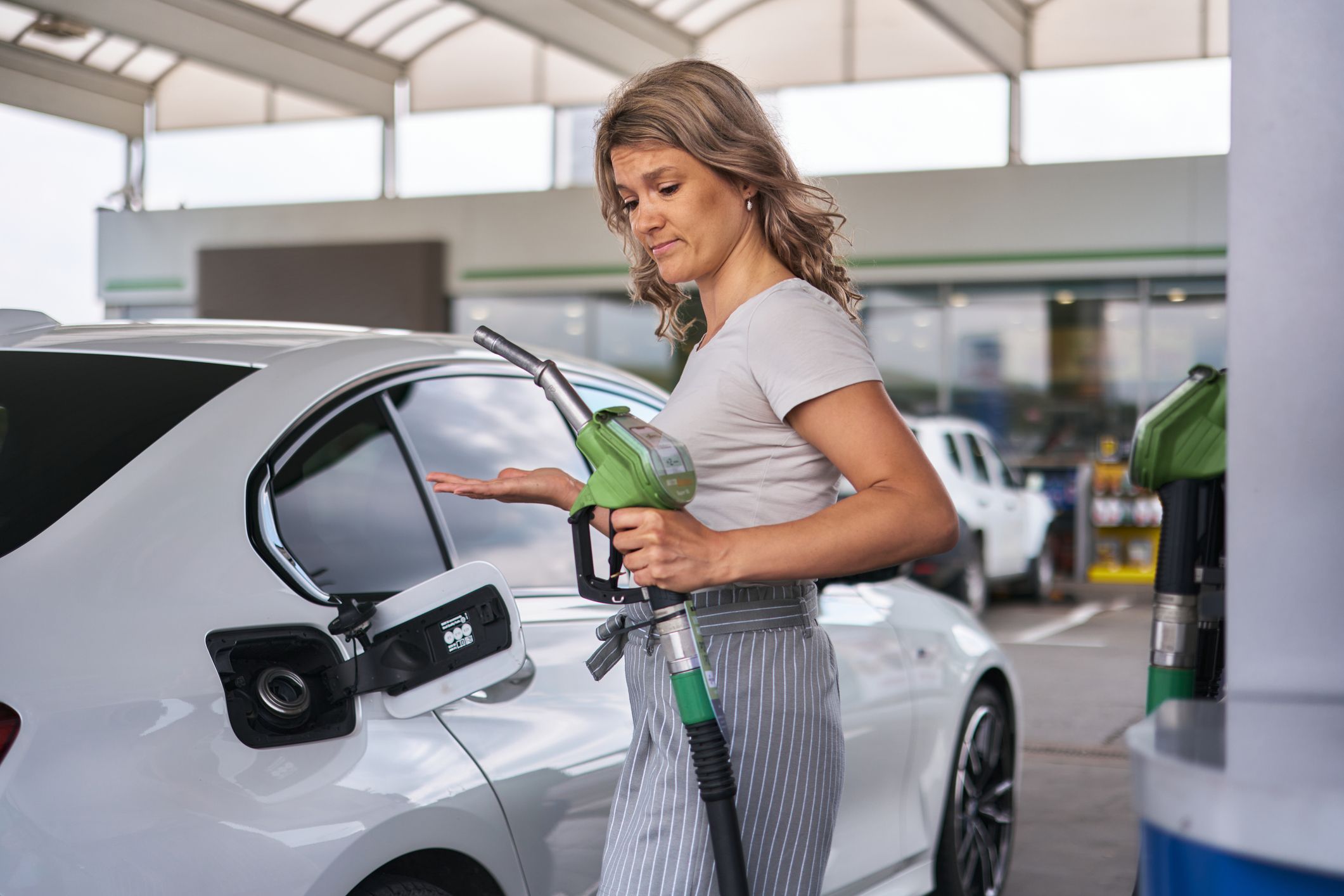 Mid adult woman feeling unsure of how to use fuel pump to refill her car at gas station
