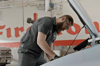 Male Firestone techician inspecting engine under the hood