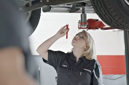 Techincian inspectng the chassis of a car with a flashlight.
