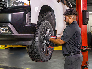 A technician using a drill to secure a wheel back onto a vehicle.