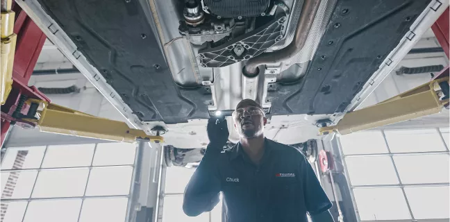 Techincian inspecting the chassis of a car with a flashlight.