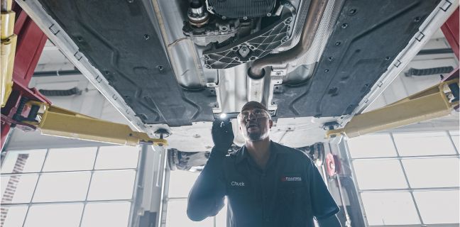 A technician inspecting the chassis of a vehicle that is lifted up in a garage.
