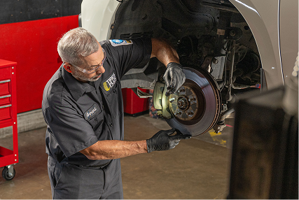 A technician inspecting the wheel axle of a lifted vehicle in a pro garage.