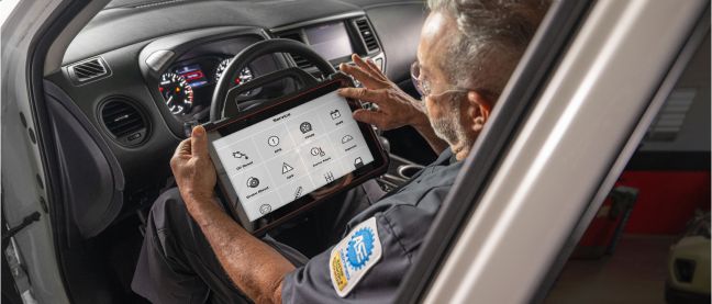 An auto technician reviewing vehicle inspection details on a tablet.