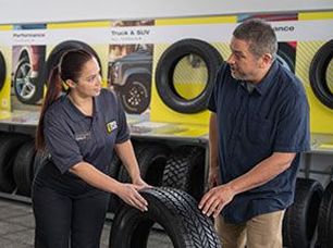A Tires Plus technician talks to customer about tire options infront of tire type display.
