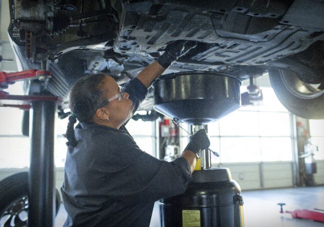 A technician working under chassis of a vehicle that is lifted up in a garage.