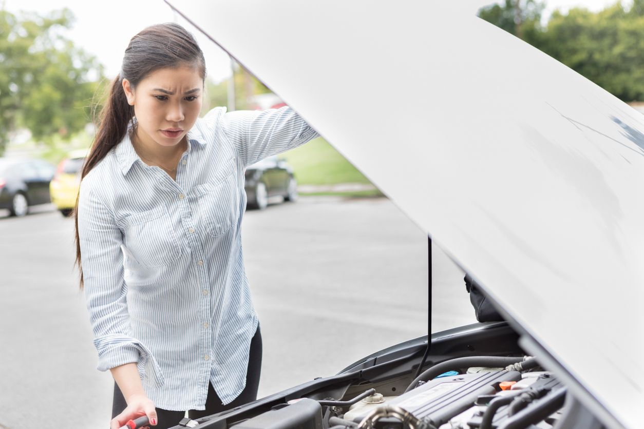 Woman checking car battery under the hood of a car