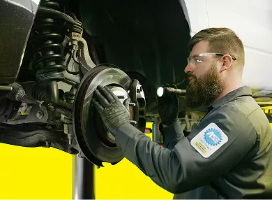 A technician using a flashlight to inspect the brakes on a vehicle.