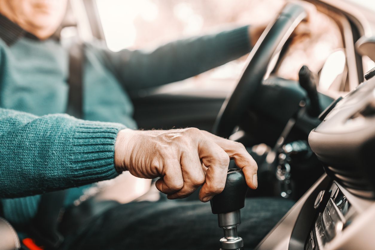 Man sitting in driver's seat of vehicle with seatbelt on reaching for gear shift