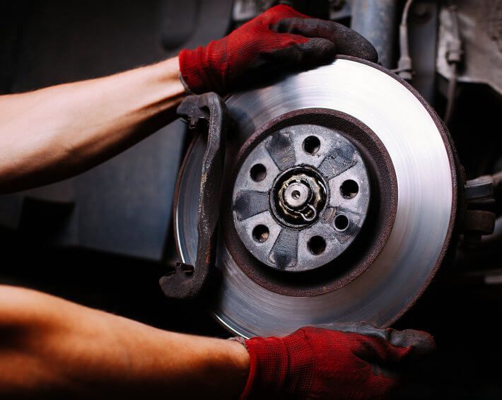 Firestone Complete Auto Care technician's red gloved hands performing a brake repair service