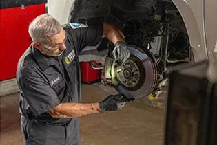 A technician inspecting the wheel axle of a lifted vehicle in a pro garage.