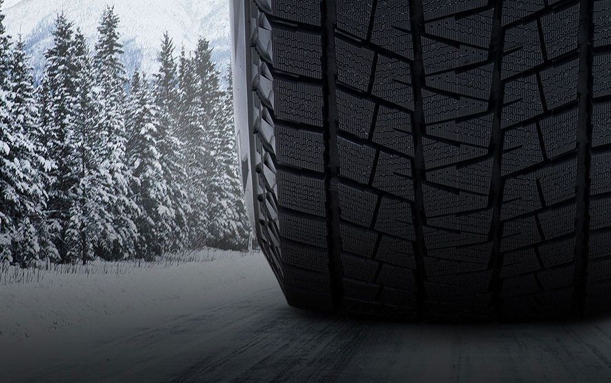 Close up of Bridgestone's Blizzak winter tire, going down a snowy road with snow-capped trees ahead