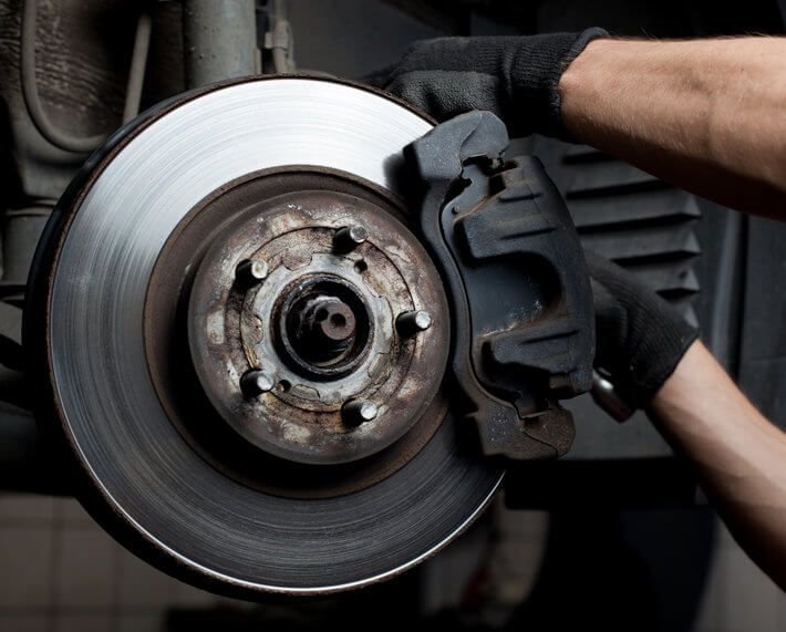 Close up of car's rotor with brake pad and mechanic's hands working