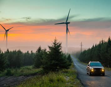 Car driving down foggy road at dawn with wind turbines in the background