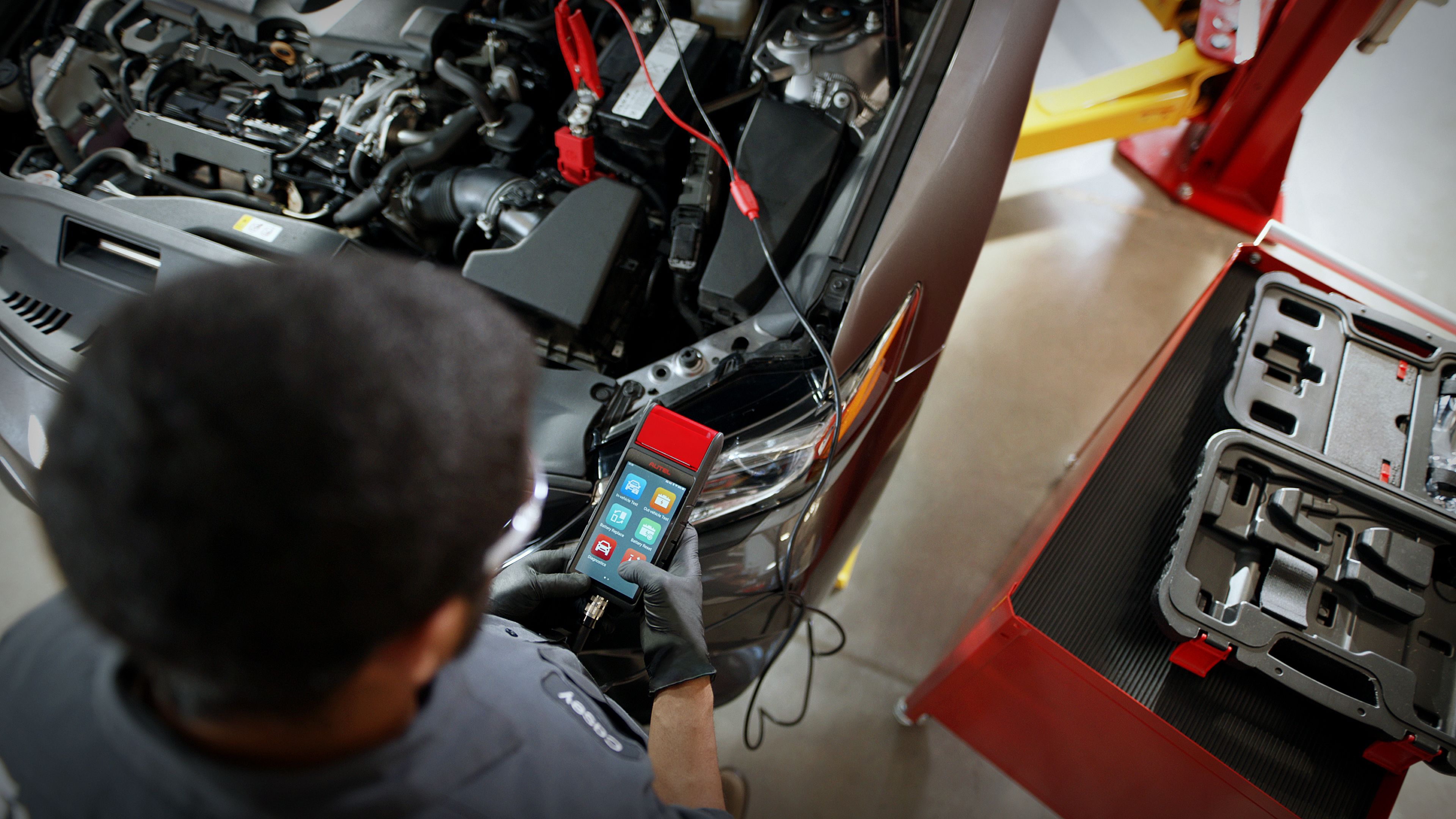 mechanic with short dark hair and safety goggles inspecting a car battery