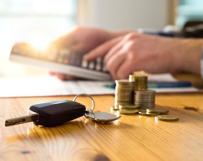 Car keys and a stack of coins on a table while a man types on a calculator